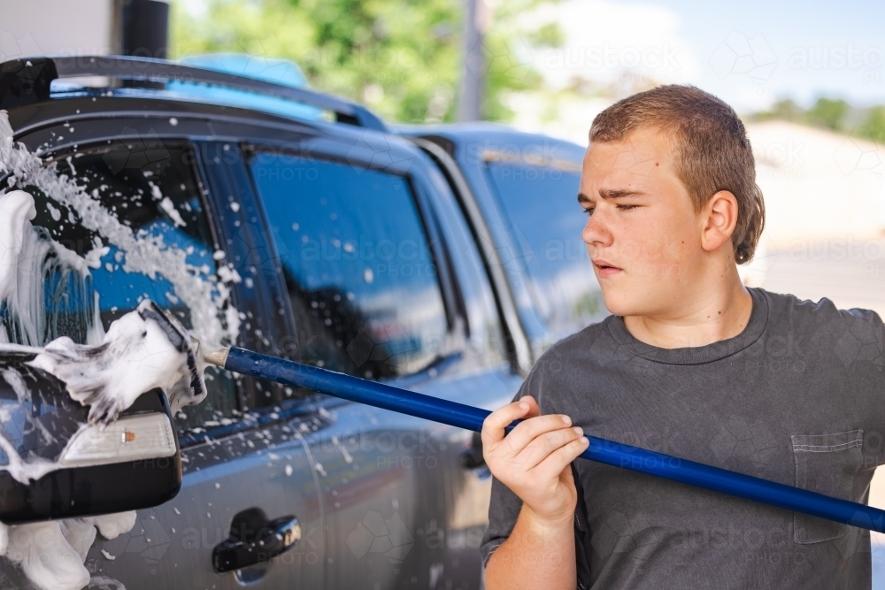 Teen boy washing vehicle in self-service car wash bay - Australian Stock Image