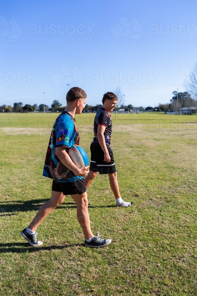 Teen boys walking off footy field after playing game holding football - Australian Stock Image