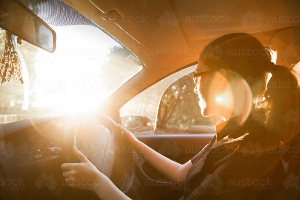 Teen girl driving car with lens flare - Australian Stock Image