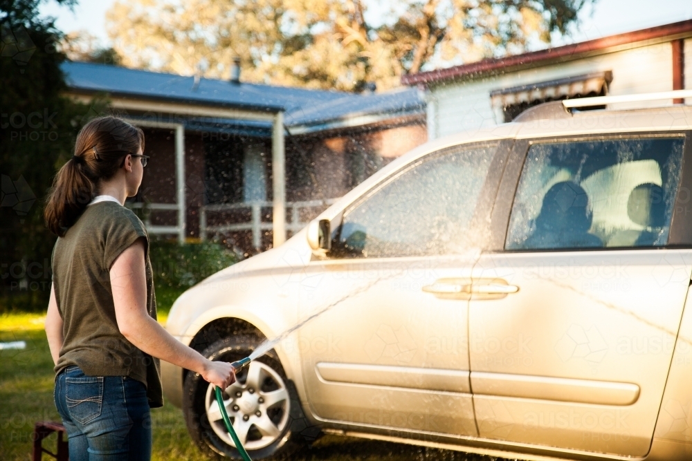 Teen girl hosing down car in the backyard - Australian Stock Image