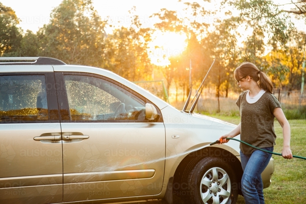 Teen girl hosing down car in the backyard - Australian Stock Image