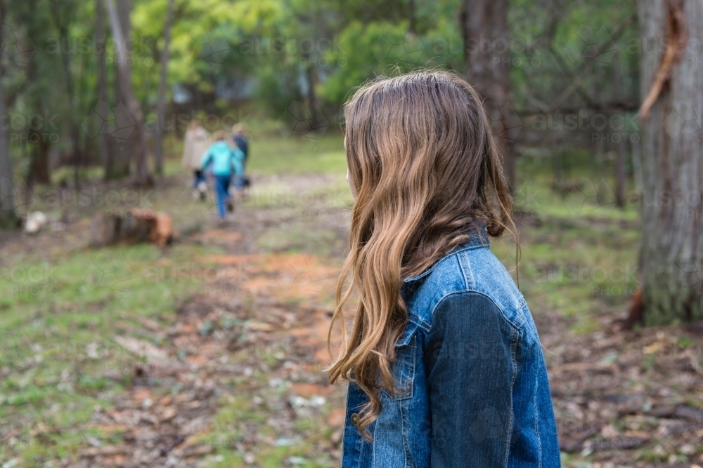 teen girl lagging behind a group of kids in a forest - Australian Stock Image