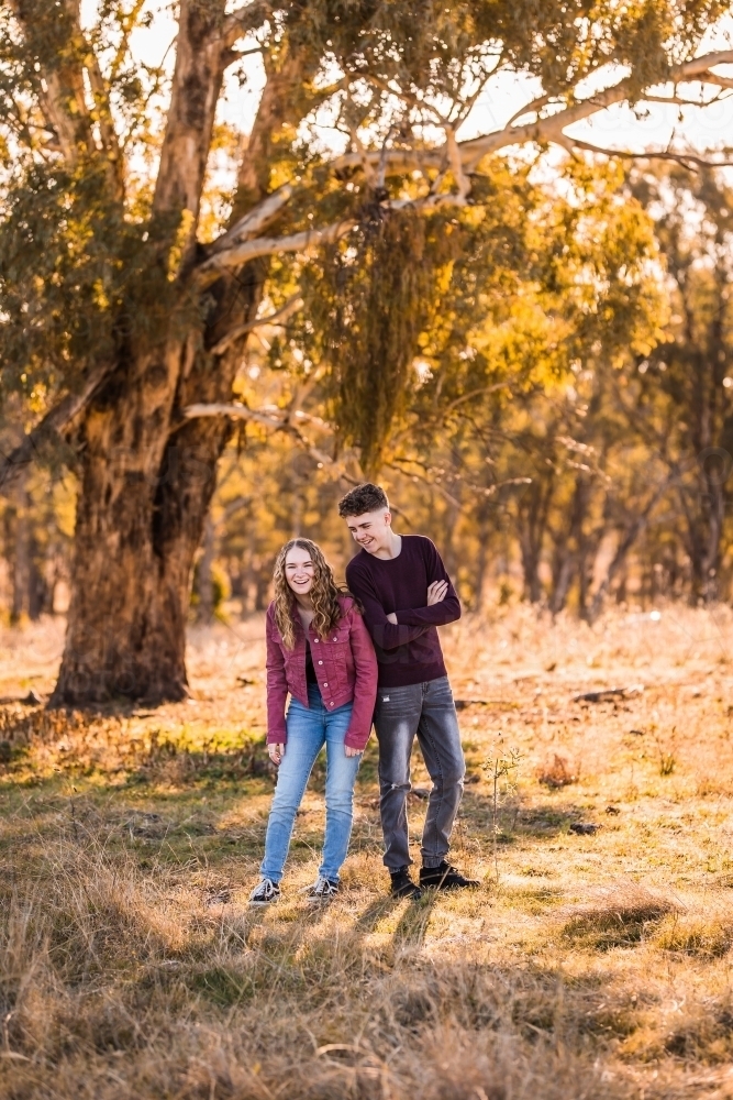 Teen girl laughing at teen boy outside in paddock on farm - Australian Stock Image