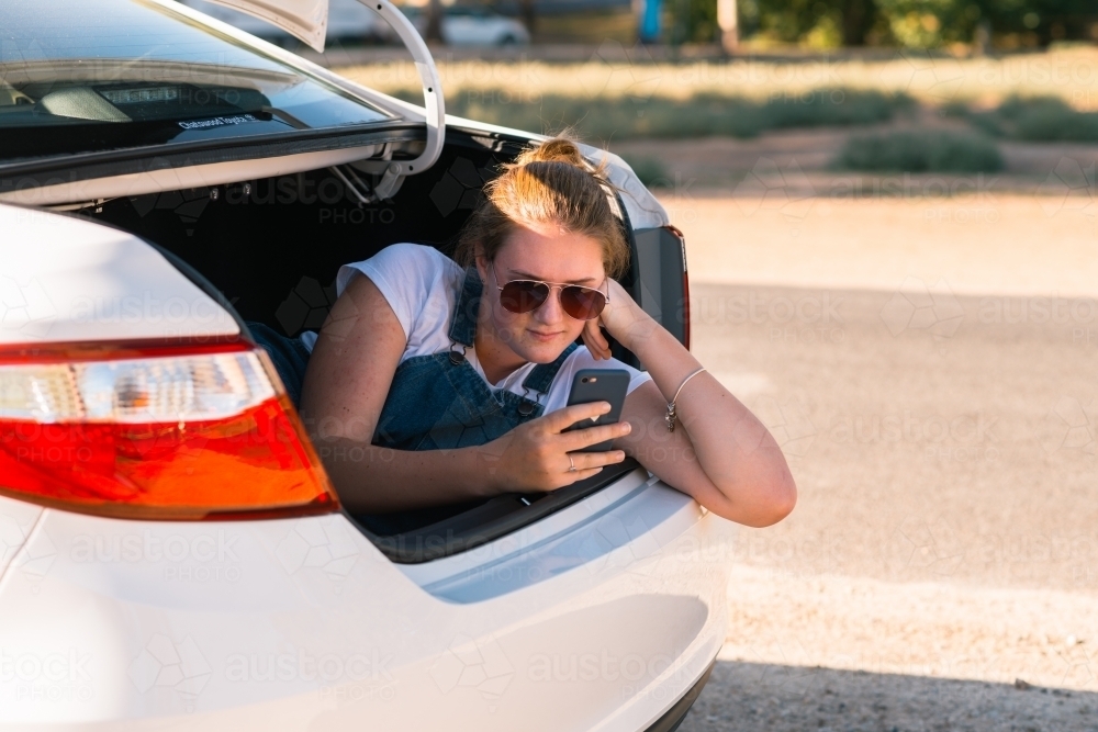 teen girl sitting in boot of car on a road trip - Australian Stock Image