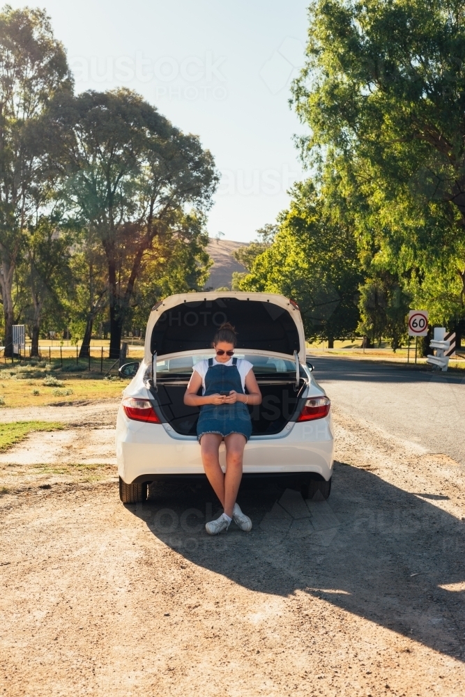 teen girl sitting in boot of car on a road trip - Australian Stock Image