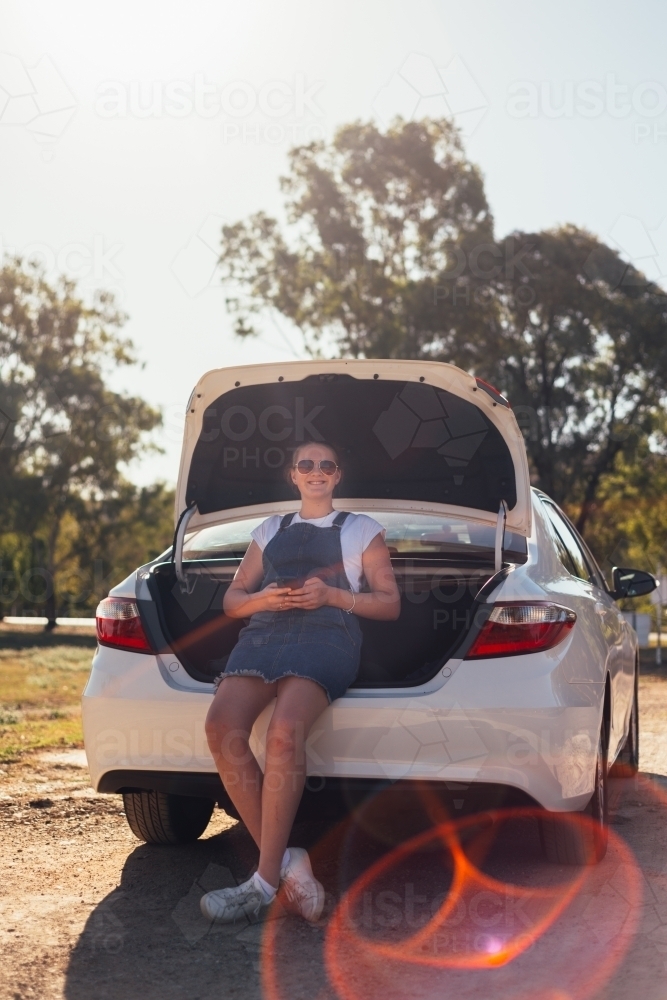 teen girl sitting in boot of car on a road trip - Australian Stock Image