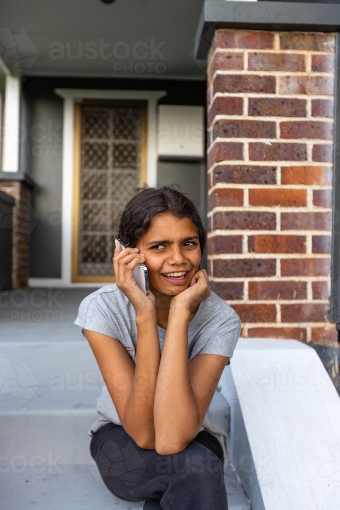 teen girl sitting on step holding mobile phone to her ear - Australian Stock Image