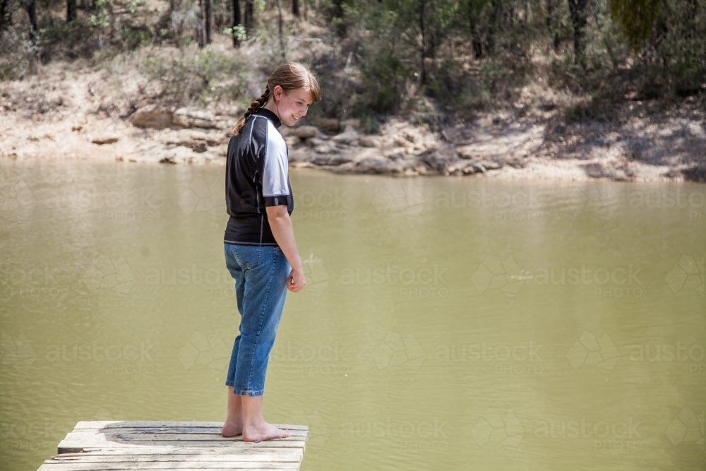 Teen girl standing on a dam wooden jetty near a country dam - Australian Stock Image