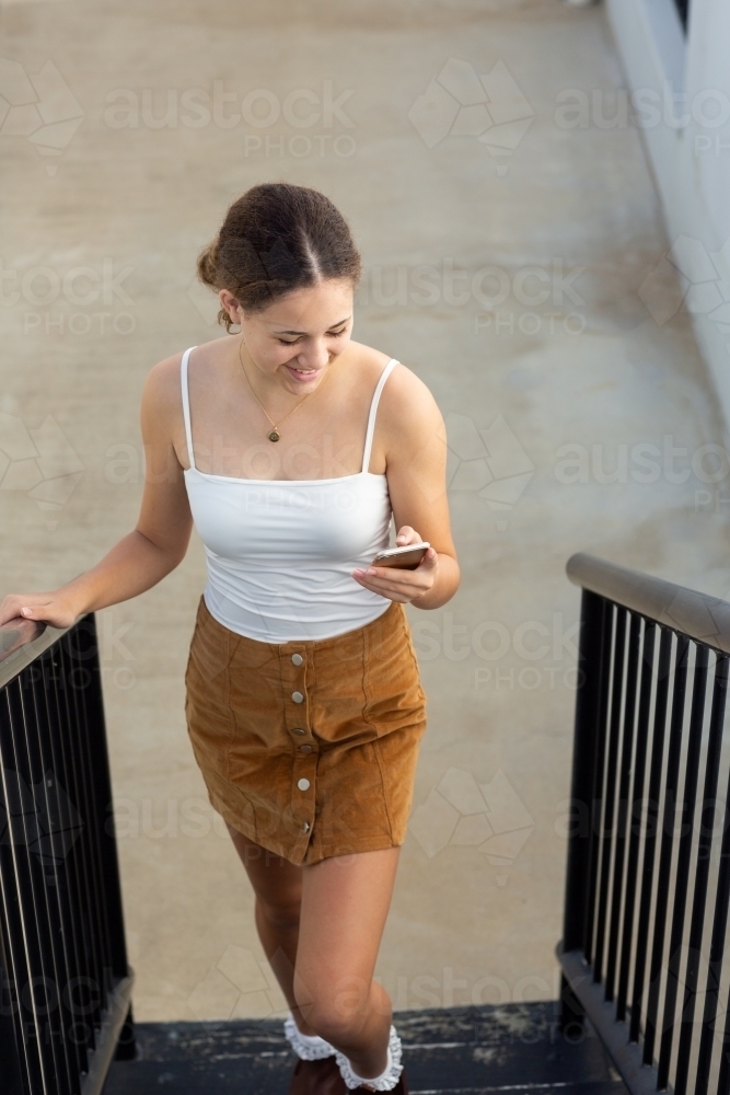 Teen girl walking up stairs while looking at smartphone - Australian Stock Image