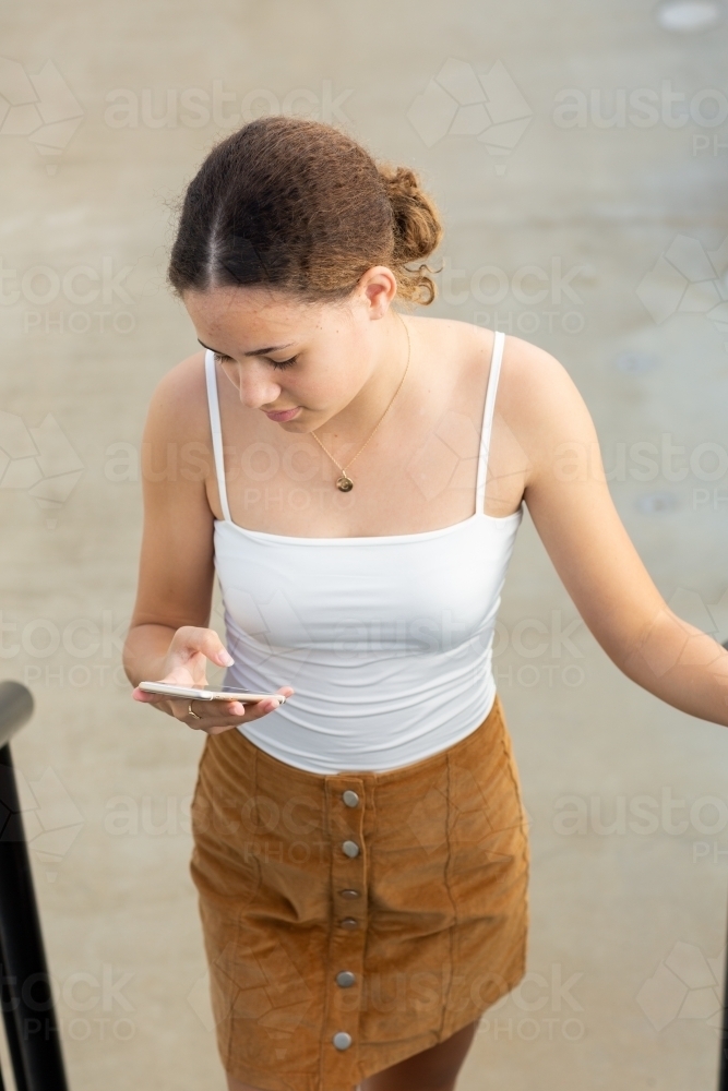 Teen girl walking up stairs while looking at smartphone - Australian Stock Image