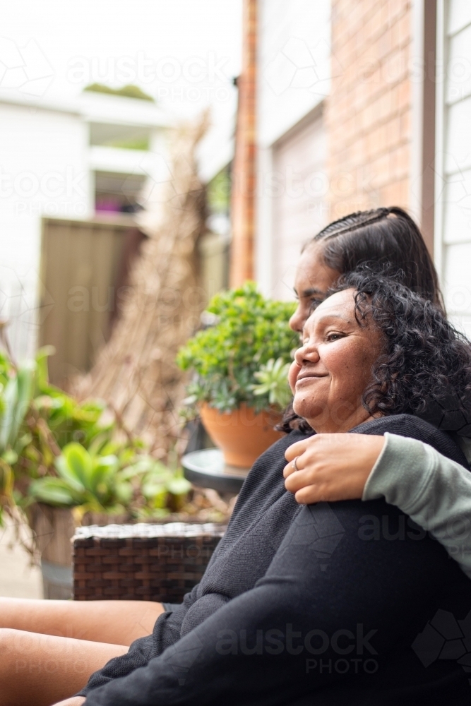 Teenage Aboriginal girl siting with her mum together on a garden bench - Australian Stock Image