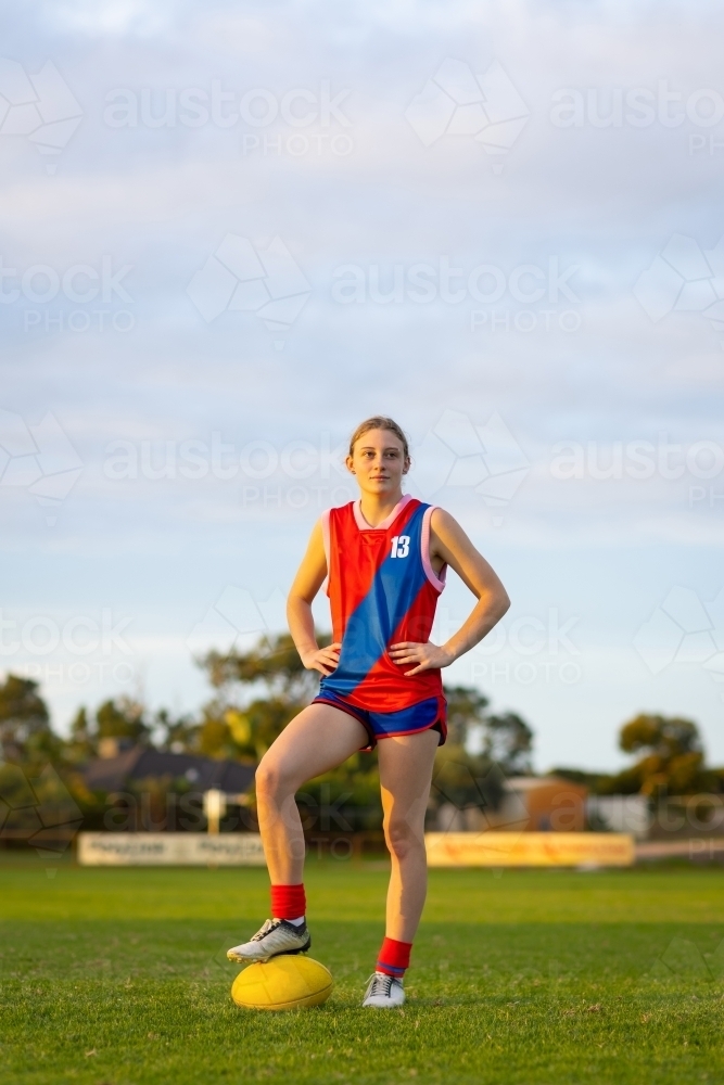 teenage aussie rules footballer standing with hands on hips and one foot on ball - Australian Stock Image