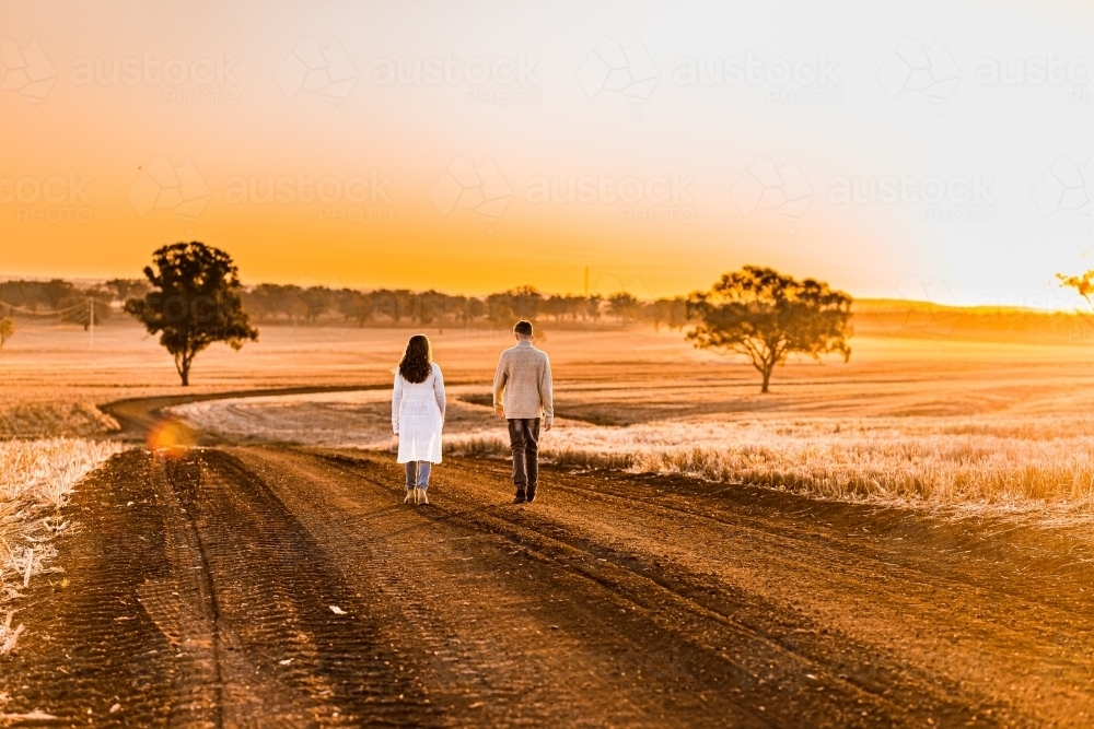 Teenage boy and girl walking together on rural dirt road at sunset - Australian Stock Image