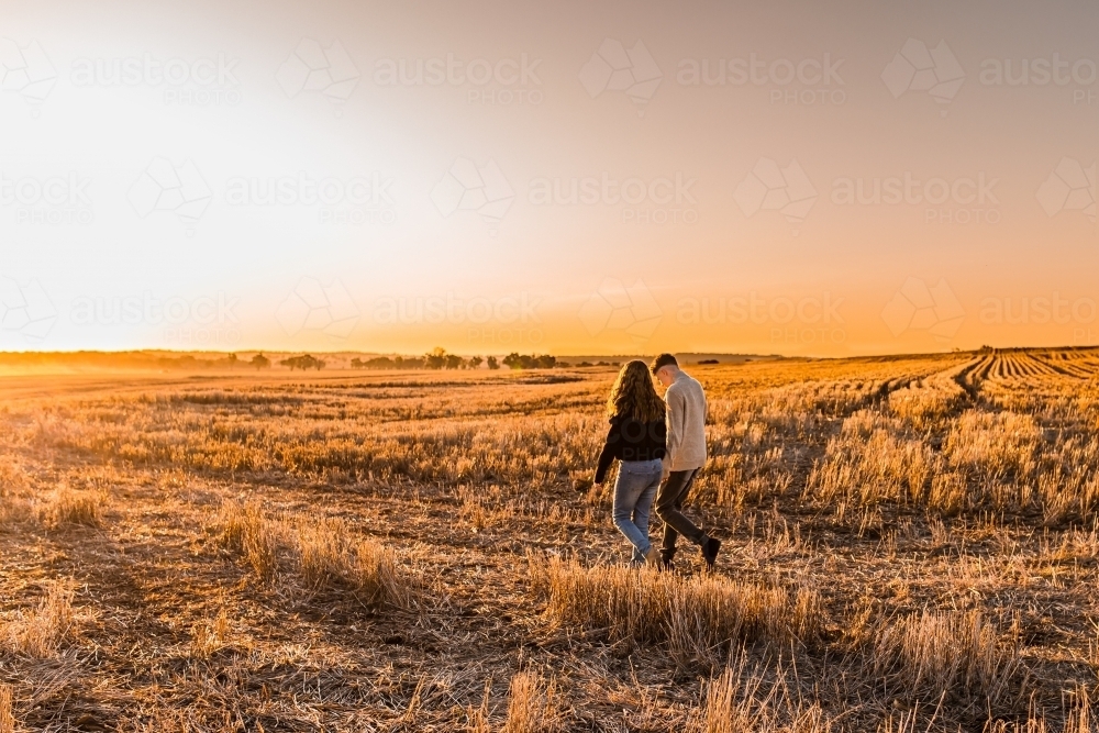 Teenage boy and girl walking together through rural grassland - Australian Stock Image