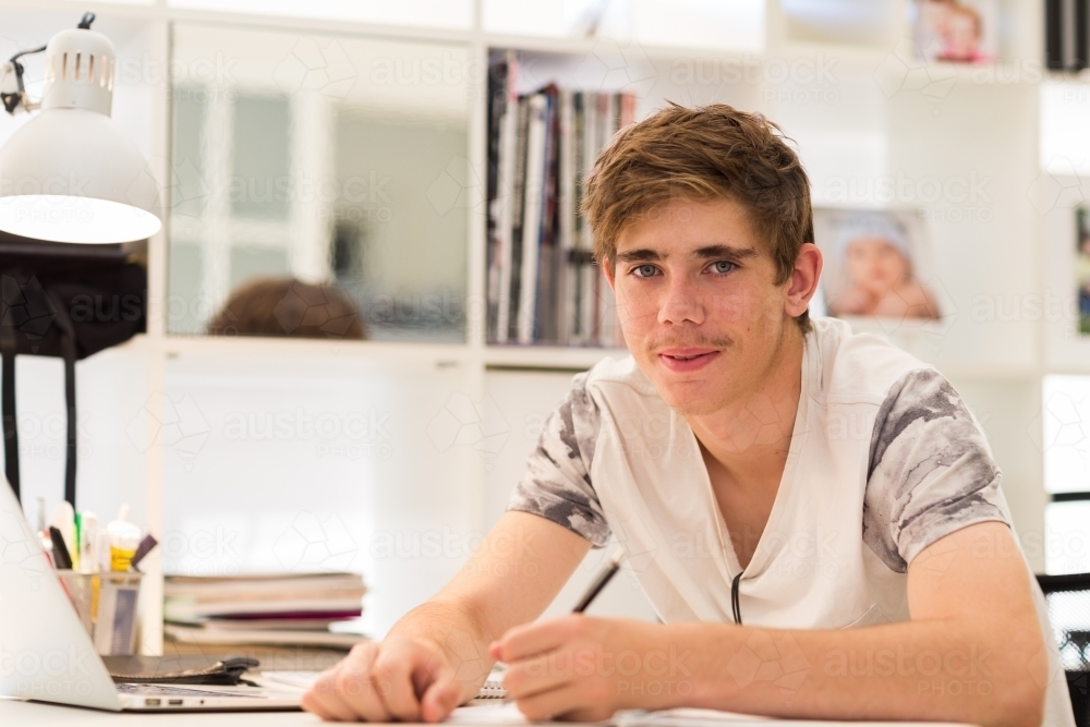 Teenage boy at desk looking at camera - Australian Stock Image