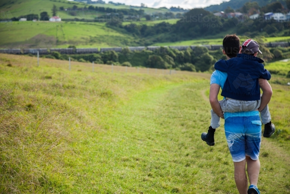 Teenage boy giving a piggyback ride to kid on a bushwalk - Australian Stock Image