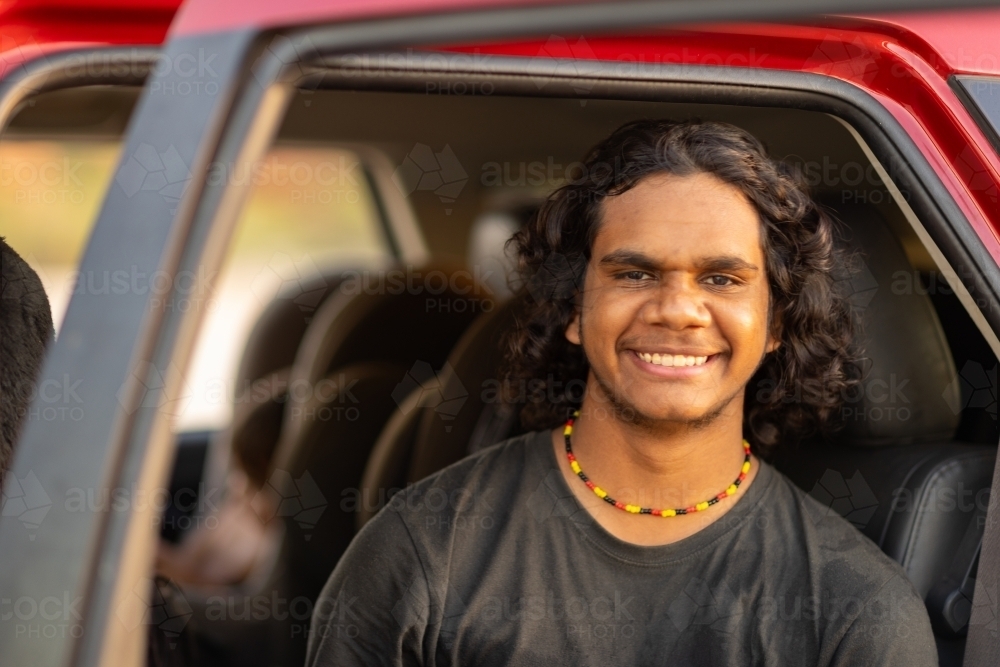 teenage boy in car smiling and looking at the camera from back seat with door open - Australian Stock Image