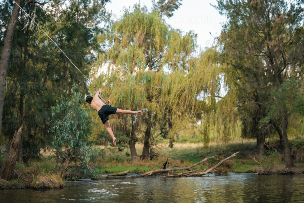 Teenage boy using rope swing at the river - Australian Stock Image