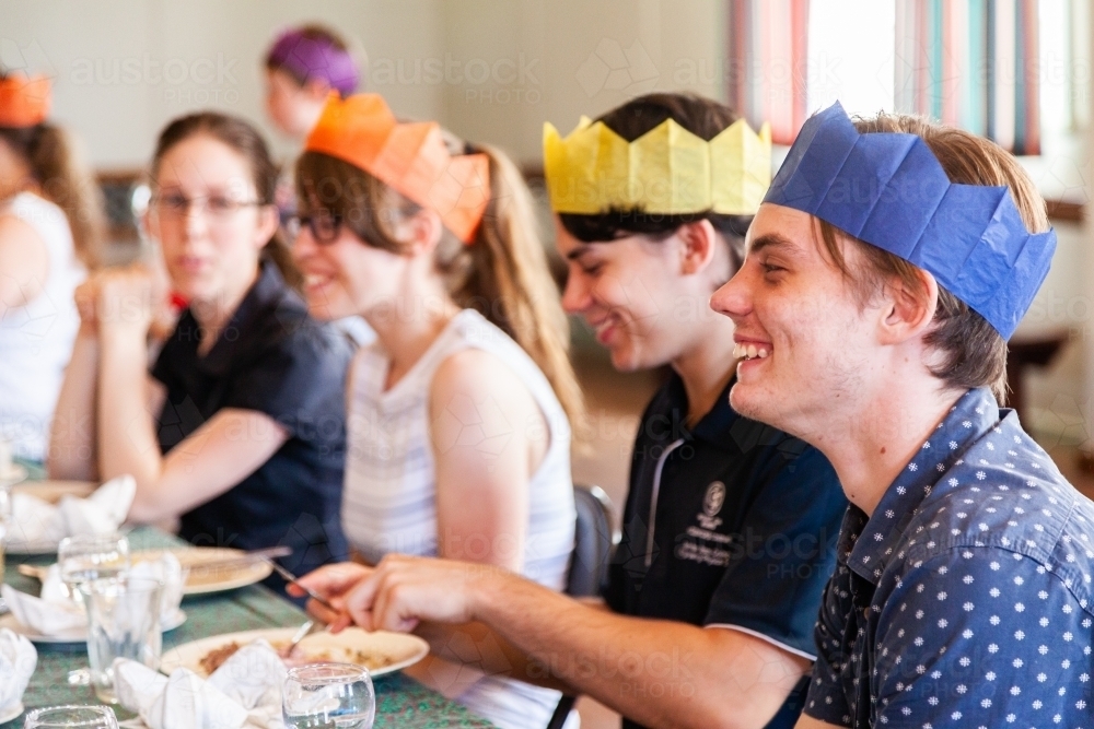 Teenage cousins laughing together at one end of the family table at Christmas lunch - Australian Stock Image