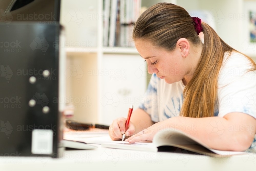 Teenage girl at desk writing notes - Australian Stock Image