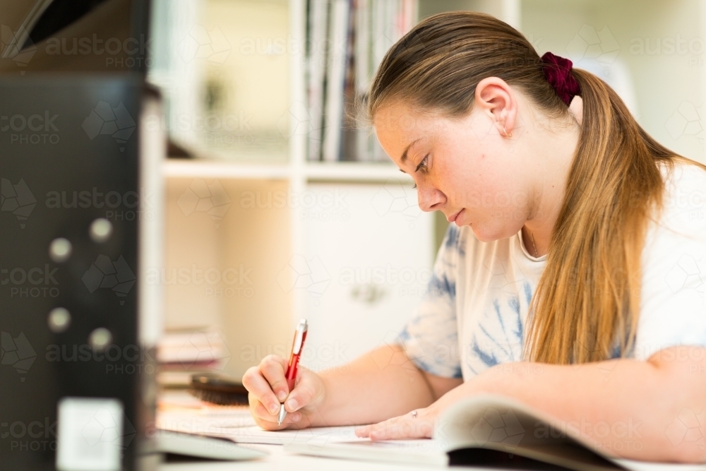 Teenage girl at desk writing notes - Australian Stock Image