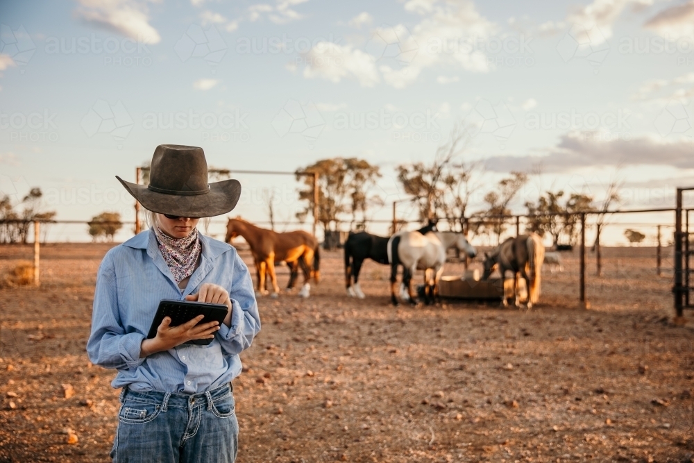 Teenage girl in brown hat using her iPad in horse yard - Australian Stock Image