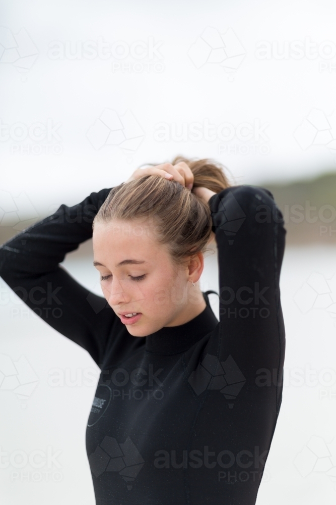 Image of Teenage girl in wetsuit tying hair into ponytail - Austockphoto