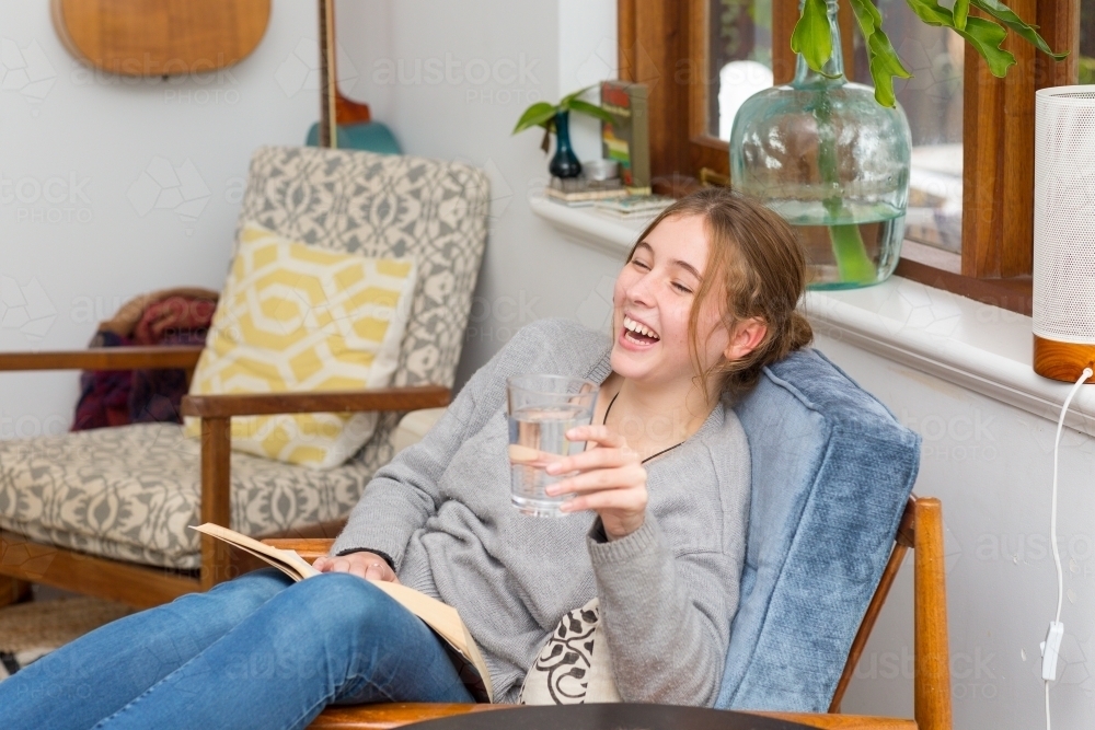 Teenage girl laughing with glass of water in hand - Australian Stock Image