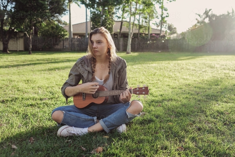 teenage girl playing ukulele in the park - Australian Stock Image