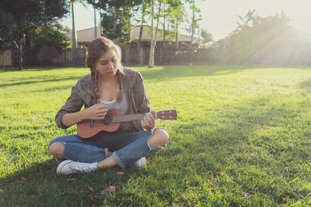 teenage girl playing ukulele in the park - Australian Stock Image