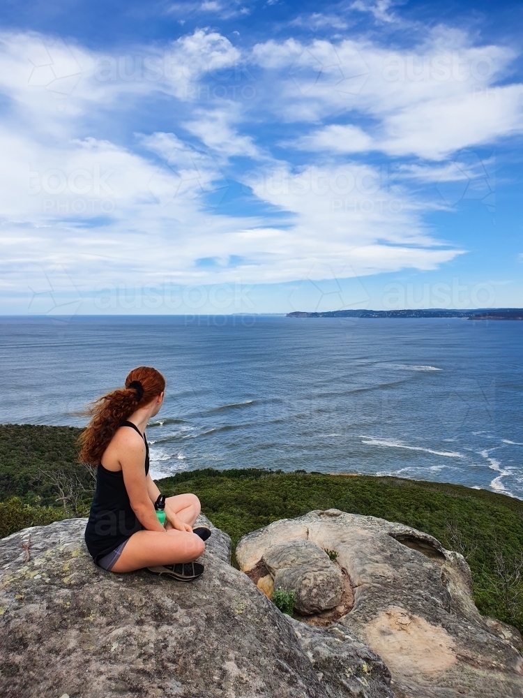 Teenage girl sitting on a rock looking out to the ocean - Australian Stock Image