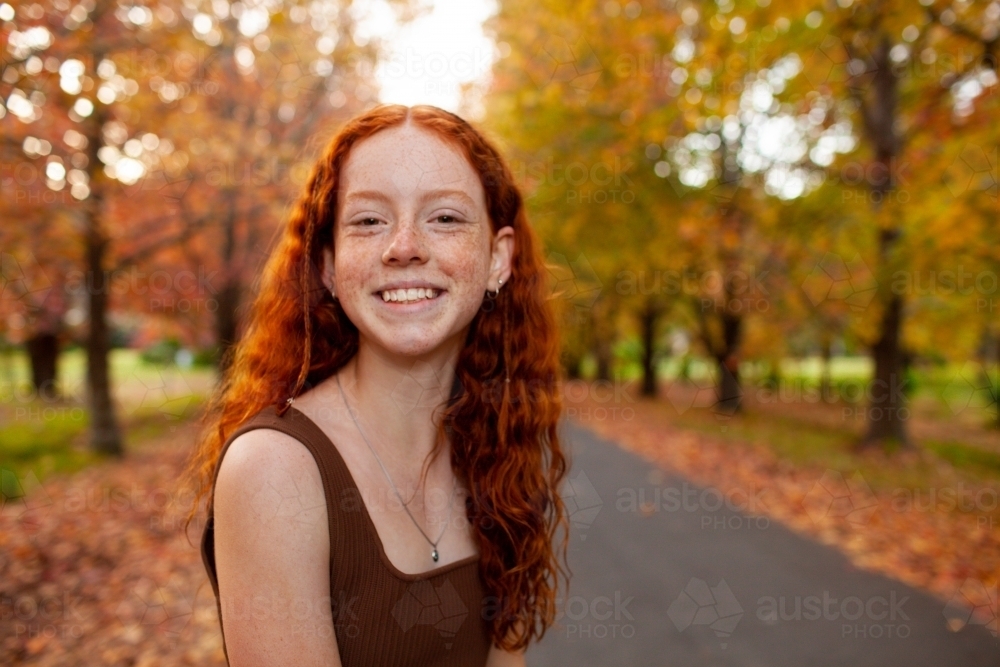 Teenage girl standing in a street lined with Autumn trees - Australian Stock Image