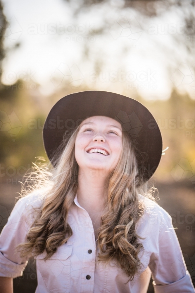 Teenage girl throwing head back laughing wearing akubra hat on farm in drought - Australian Stock Image