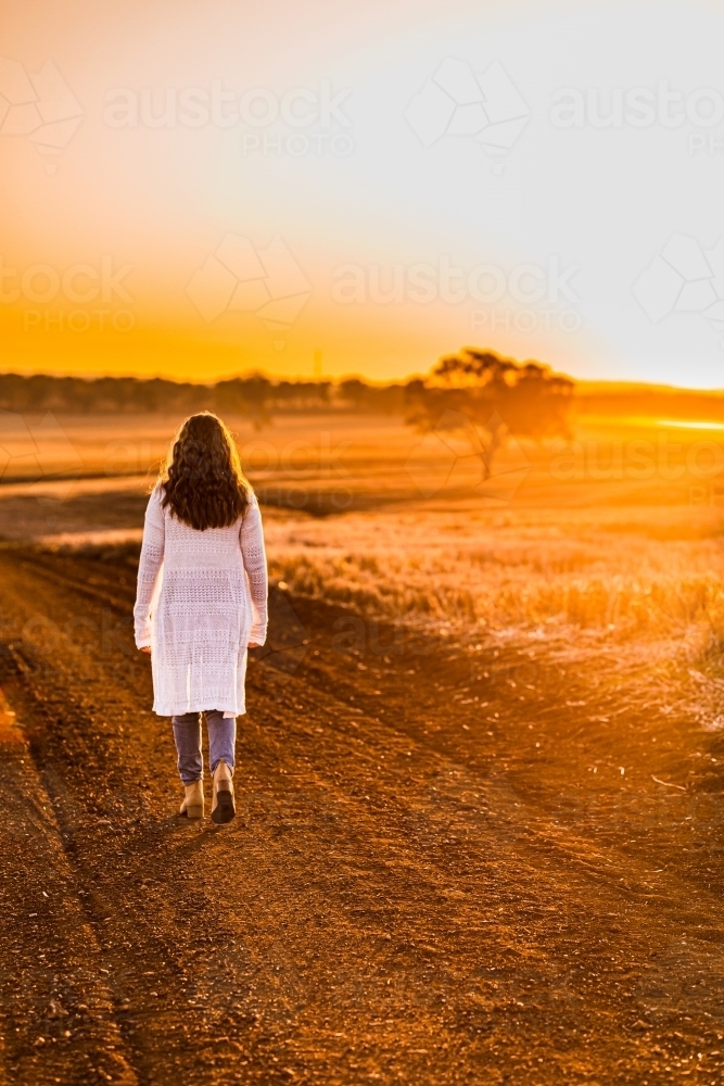 Teenage girl walking away from the camera on dirt road - Australian Stock Image