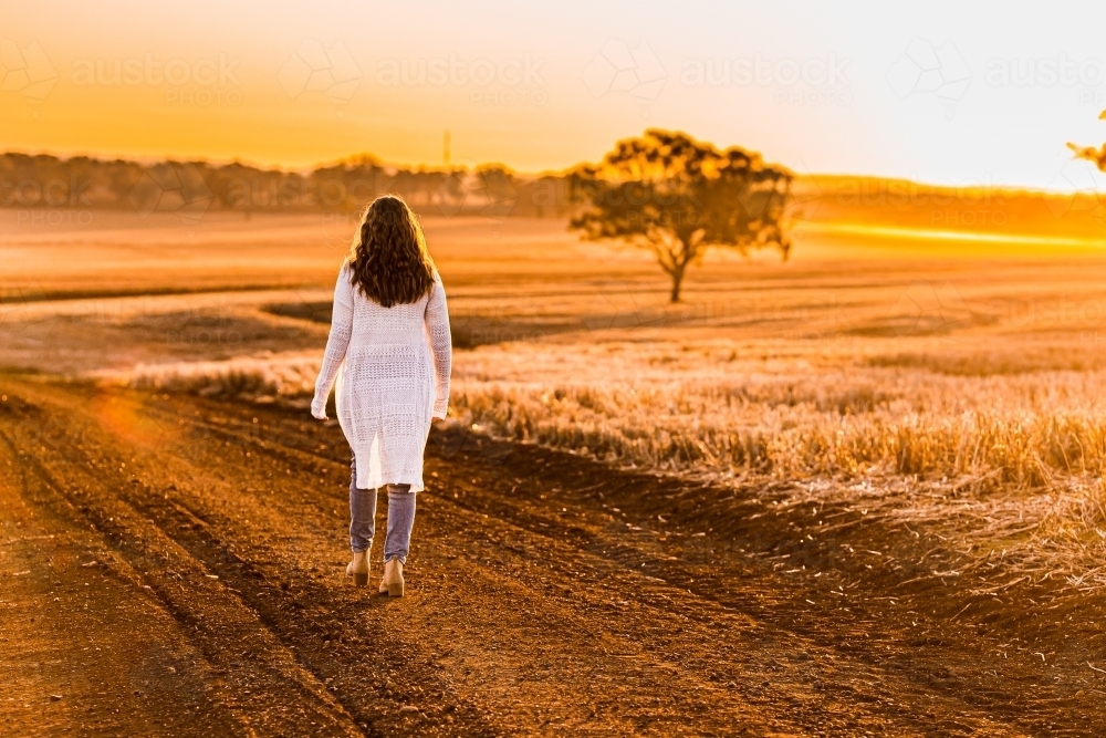 Teenage girl walking away from the camera on dirt road - Australian Stock Image