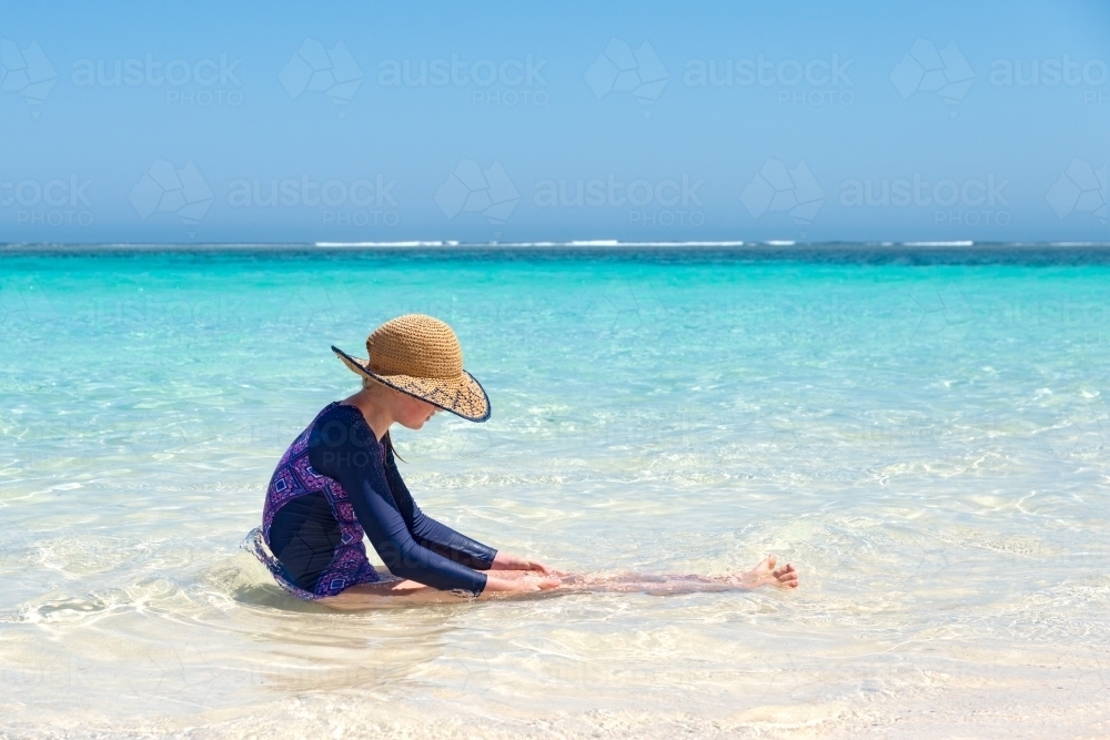 Teenage Girl Wearing Large Hat Sitting in Ocean - Australian Stock Image