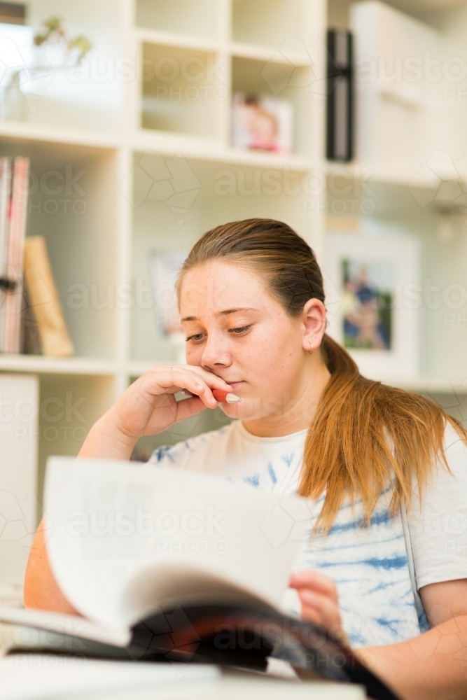 Teenage student reading a book for homework - Australian Stock Image