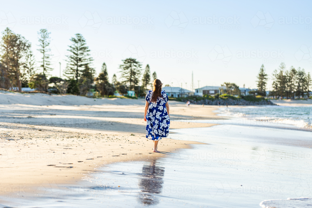 Teenaged Torres Strait Islander girl walking along coastal shoreline in traditional floral dress - Australian Stock Image