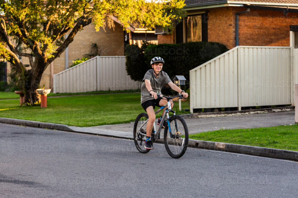 Teenager riding bike wearing helmet for safety on street in town - Australian Stock Image