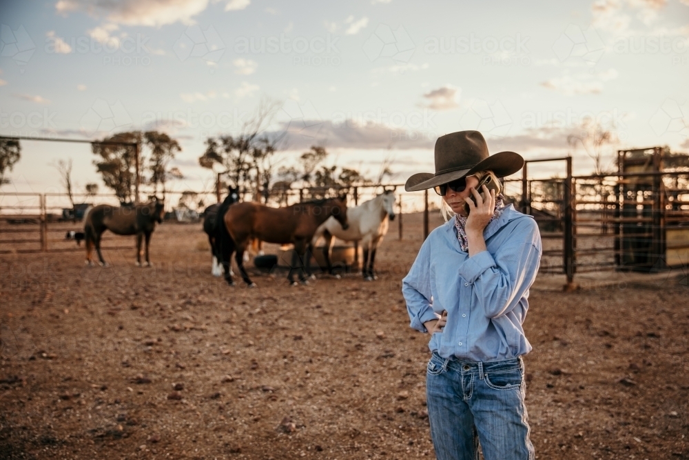 teenager standing near horses talking on her mobile - Australian Stock Image