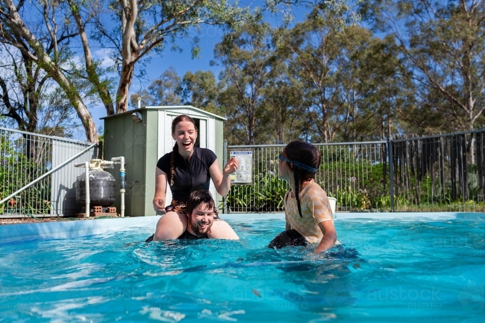 Teenagers and young adults playing shoulder wars in backyard swimming pool - Australian Stock Image