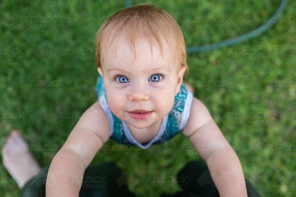 ten month old baby pulling up to stand on mums legs outside in garden - Australian Stock Image