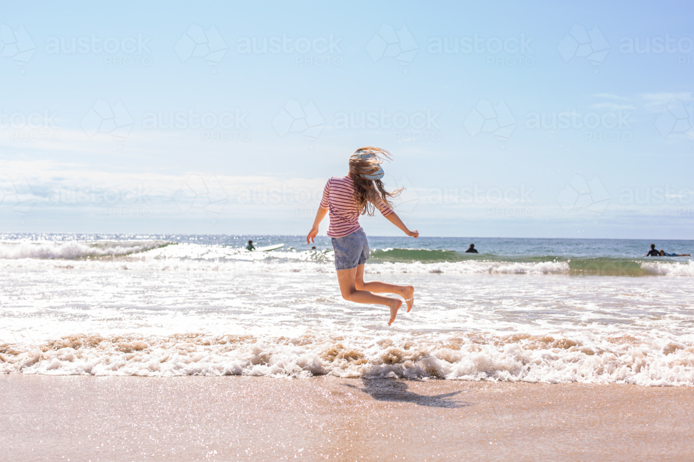 ten year old girl jumping over breaking waves at the beach - Australian Stock Image