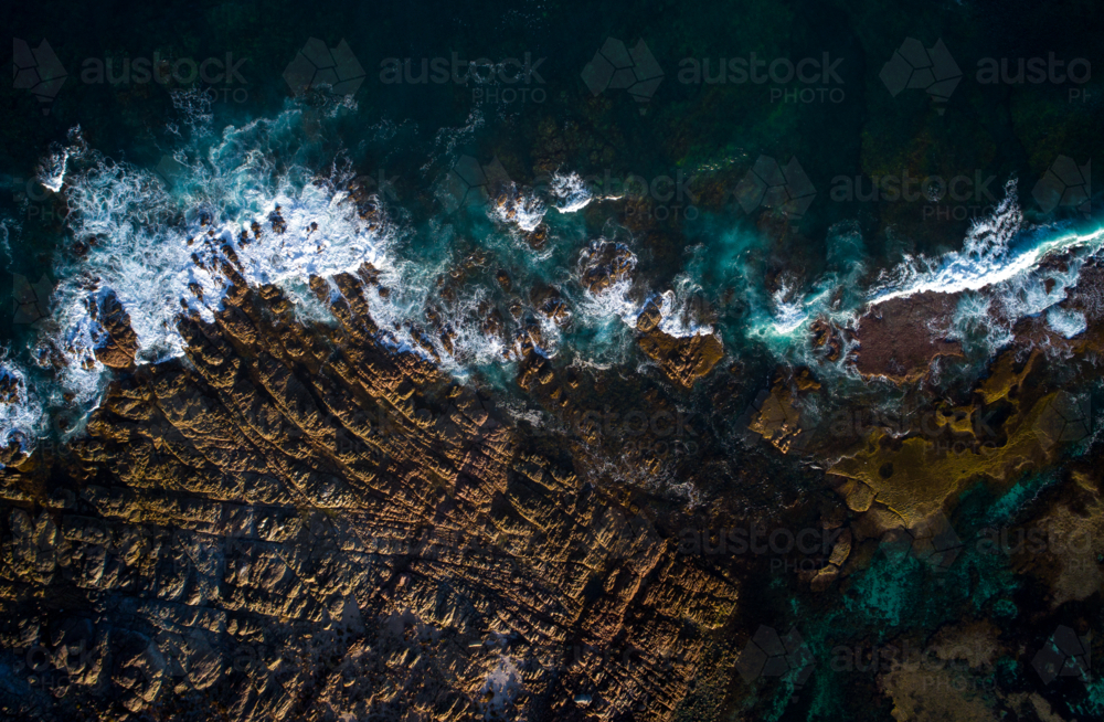 The dark ocean is kept at bay by jagged, exposed rock - Australian Stock Image