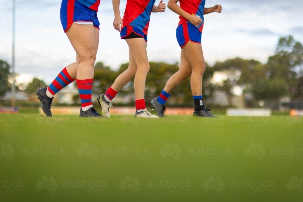 the legs of three female football players jogging onto a football oval - Australian Stock Image