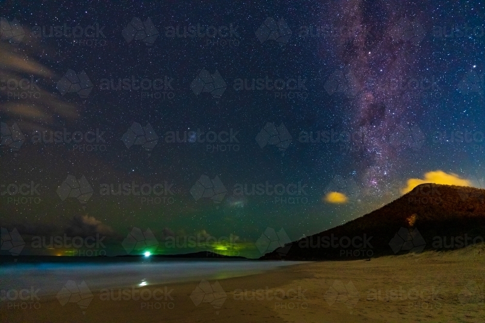 The Milky Way galaxy in the night sky over a coastal mountain at the end of a beach - Australian Stock Image