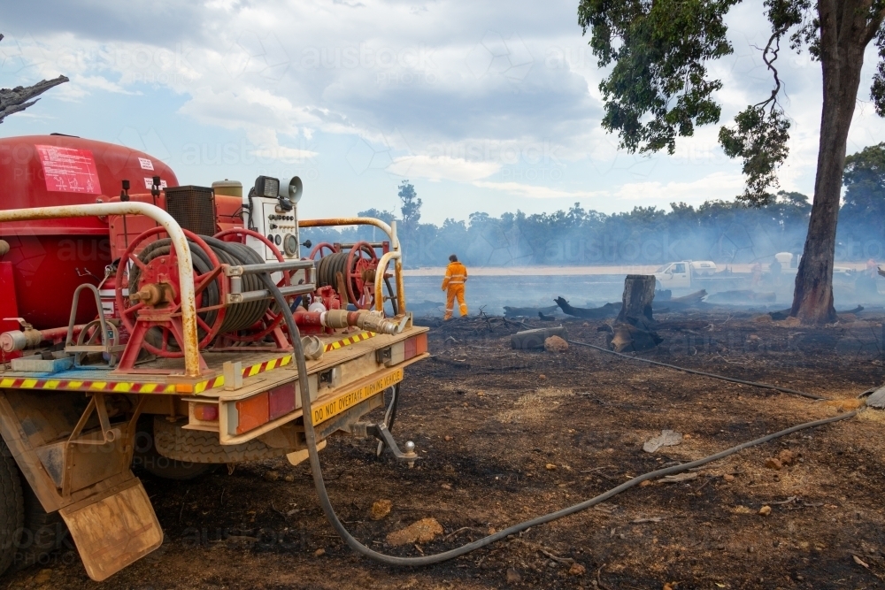 the rear of a firetruck with hoses and reels with burnt ground and smoke - Australian Stock Image