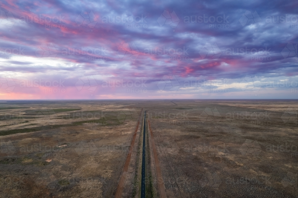 The sky is filled with pink storm clouds over a remote road with dirt tracks - Australian Stock Image