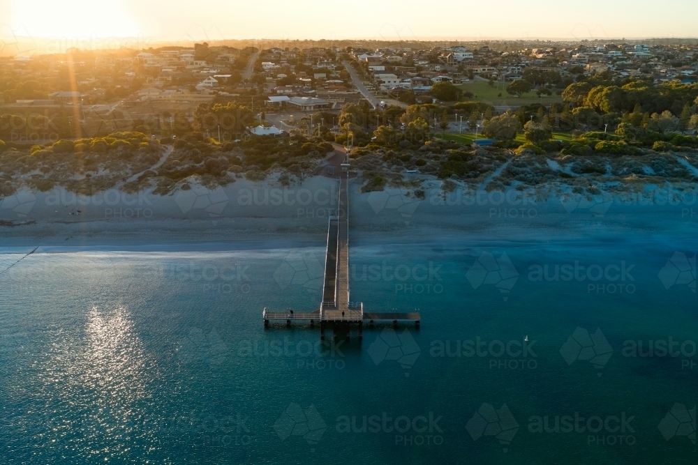 The sun rising over the horizon behind water and jetty at Coogee Beach in Western Australia. - Australian Stock Image