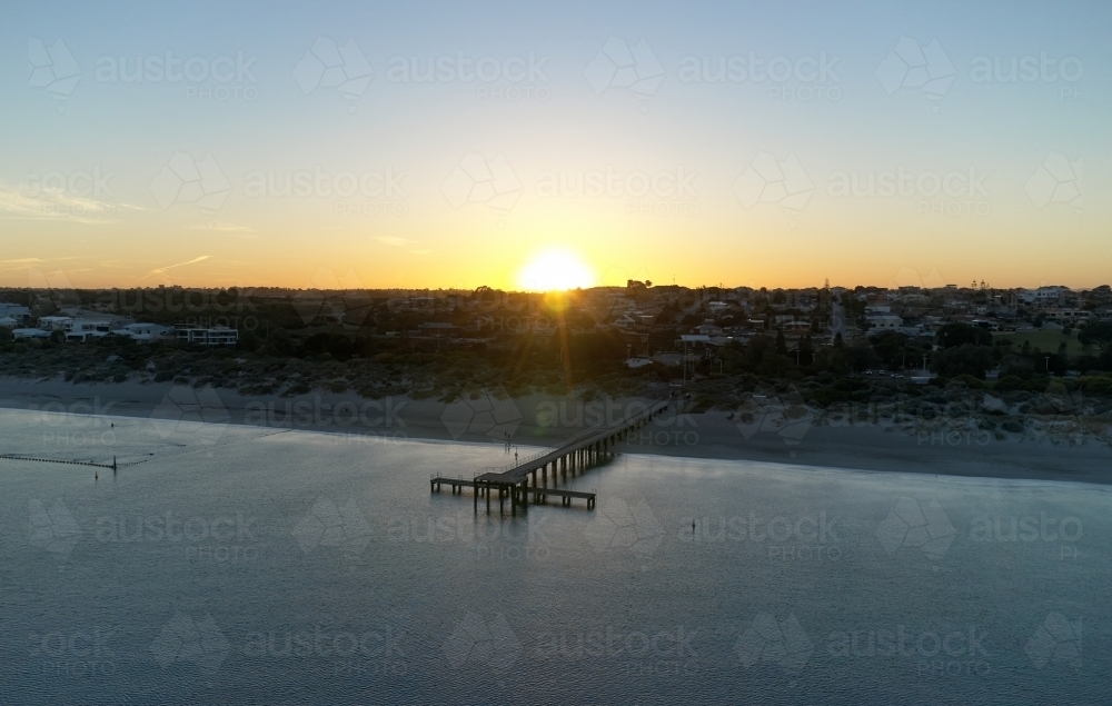 The sun rising over the horizon, with a view across the water and jetty at Coogee Beach, Perth - Australian Stock Image